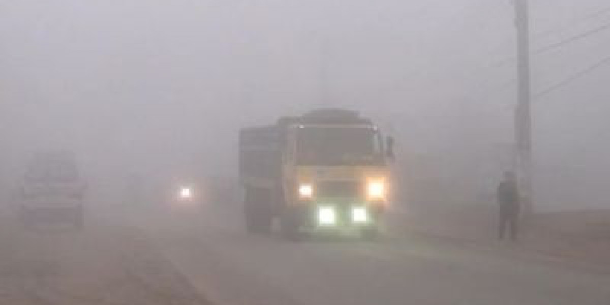 A car drives with its headlights on in dense fog.